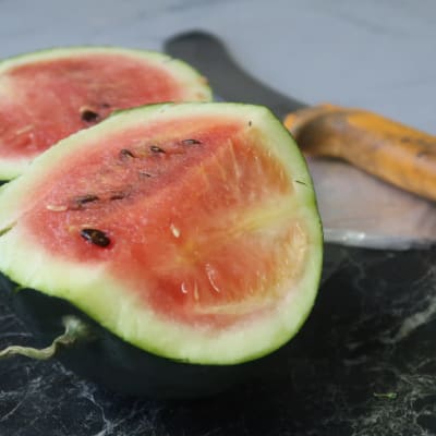 En liten uppskuren vattenmelon på ett bord, en kniv i bakgrunden.