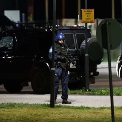 En tungt beväpnad polis står vid ett par polisbilar.