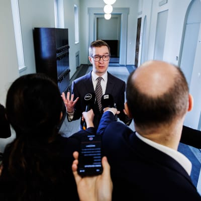 Oras Tynkkynen omringad av journalister, mikrofoner och kameror.