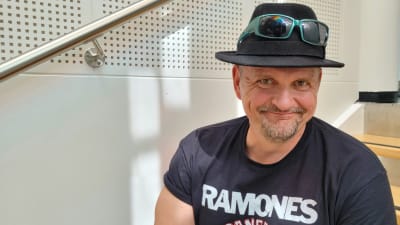 Klamydia-bändin laulaja Vesku Jokinen istuu portailla hattu päässään ja hymyilee.