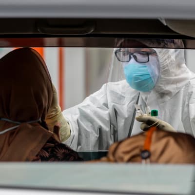 En person som sitter i en bil testas för coronaviruset av en vårdare klädd i skyddsutrustning.