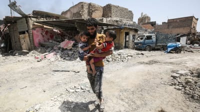 Man bär på två barn mitt bland ruiner i Mosul.