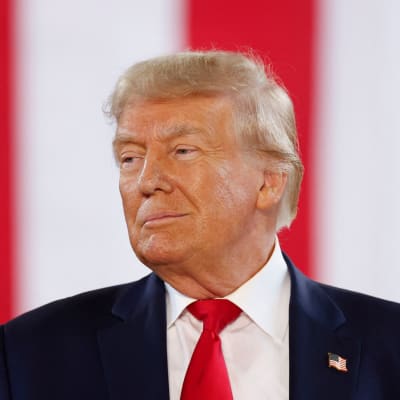Donald Trump i närbild framför en rödvitrandig bakgrund. På kavajuppslaget har han en pins formad som en amerikansk flagga.