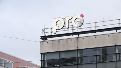 En skylt med texten "pro" ovanför på toggen av ett flervåningshus i stadsmiljö. 