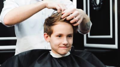 Ung kille blir klippt i en barberarstol. 