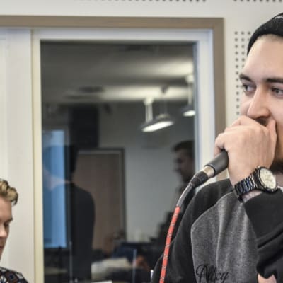 Kaksi nuorta miestä, joista toinen soittaa rumpuja ja toinen räppää mikrofoniin.