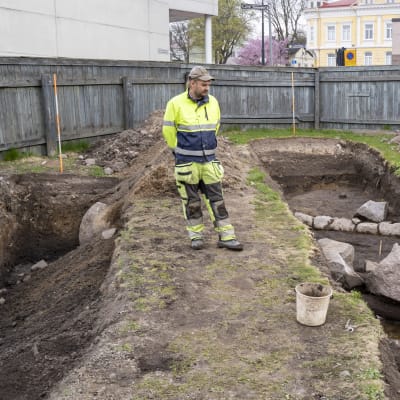 Tre personer vid en arkeologisk utgrävning i Ekenäs där man hittat stockar och stenar som varit husgrunder.