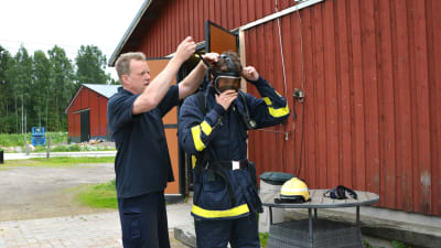 Man hjälper man i brandmansutrustning att ta på gasmask.