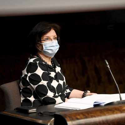 Kvinna med mörkt hår, munskydd och svartvitmönstrat plagg bakom en desk och en mikrofon i  Riksdagens generalsekreterare Maija-Leena Paavola på en presskonferens i Helsingfors den 29 juni 2021.