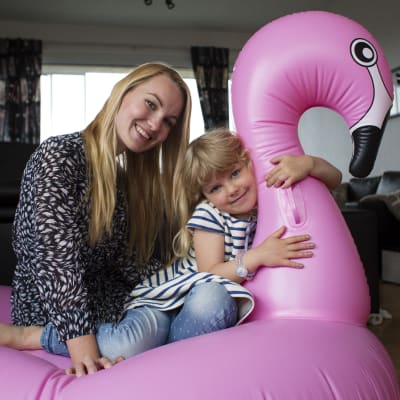 Mamma Ellen och dottern Wilda sitter på en uppblåsbar rosa flamingo i deras vardagsrum.