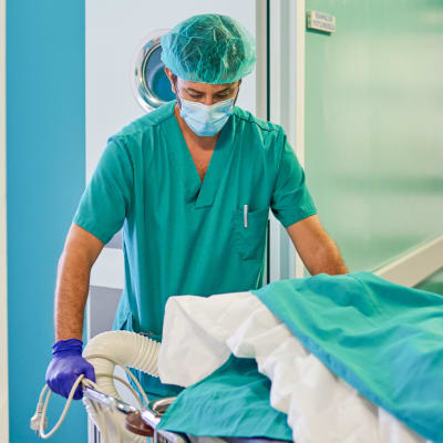 En sjukskötare i munskydd rullar runt en sjukhussäng i en korridor.