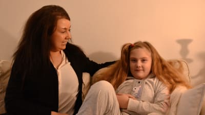 En kvinna och hennes 7-åriga dotter sitter i en soffa och ler.
