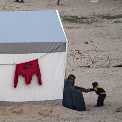 En palestinsk familj utanför ett tält med Röda halvmånens skära på taket. Vid tältväggen hänger kläder på tork.