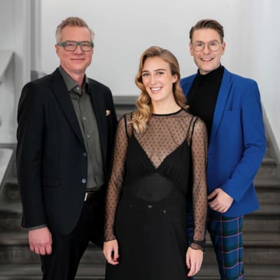 Programledarna Mårten Svartström, Siri Fagerudd och Thomas Lundin poserar leende för kameran i en trappa. 