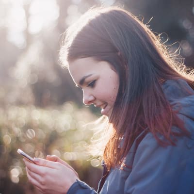 Flicka ser på sin smarttelefon ute i skogen.