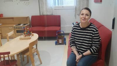 Kvinna i randig tröja sitter på en röd soffa.