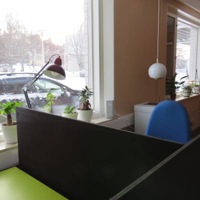Ett litet kontor för distansjobb. Kontorsstol, arbetsbord, en printer i bakgrunden. Fönster med snölandskap ute.