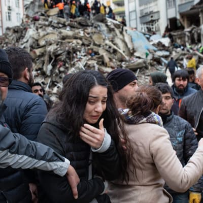 En kvinna gråter framför en rasad byggnad.