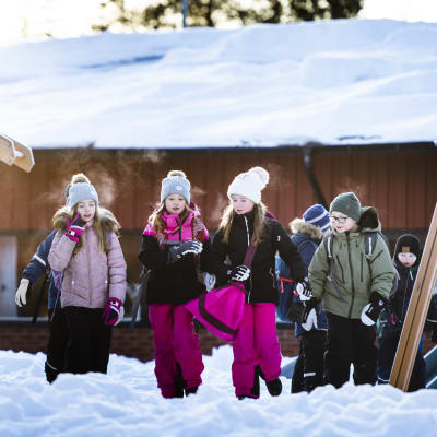 Barn i rad på solig skolgård med snö. 