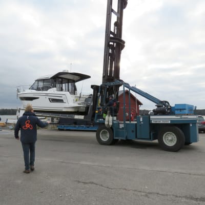 En motorbåt uppe på en truck. En man med ryggen mot kameran följer med. Vinterupptagning av båt.