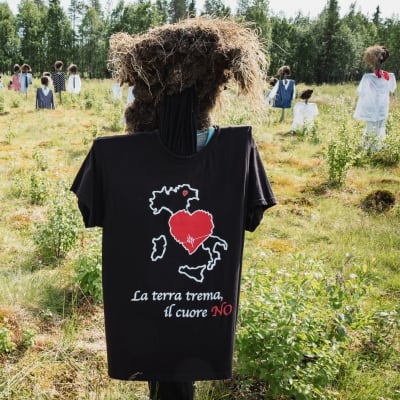 Hiljainen kansa -teoksen heinäseiväshahmo, jolla musta t-paita, jossa italiankielinen teksti La terra trema, il cuore no.