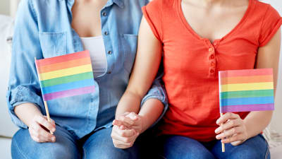 två kvinnor håller varanra i handen och håller i varsin regnbågsflagga