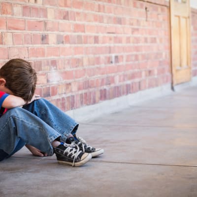 Ett barn ser ut att vara ledsen och sitter i en korridor och täcker sitt ansikte med armarna.