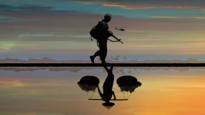 Soldat i solnedgång med helikopter i bakgrunden.