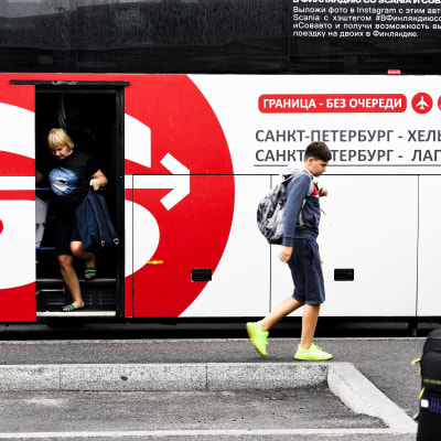 En ung man med ryggsäck stiger av en rödvit buss med kyrilliska bokstäver. Bussen för resenärer från St. Petersbrug till Helsingfors-Vanda flygplats. 