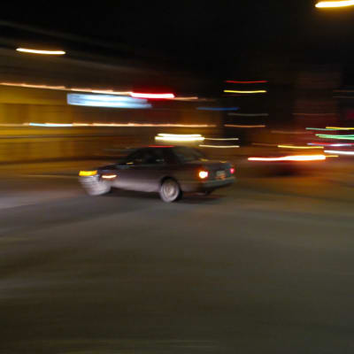 En bil kör i en stad när det är mörkt. Konturerna på bilden är suddiga.