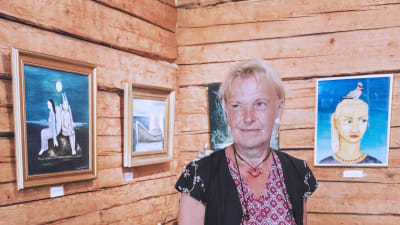 Taiteilija Stina Engvall kuvattuna Galleria Gottorpissa, taustalla hänen maalauksiaan seinällä.