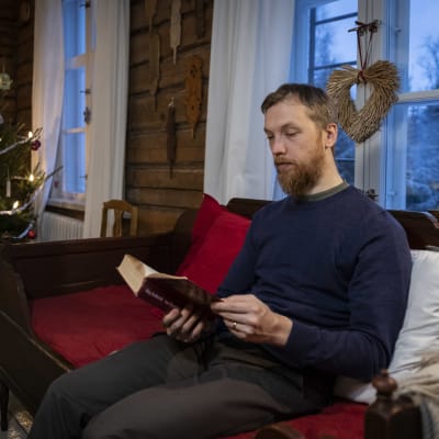 Mikko Nikkilä lukee kirjaa. Taustalla näkyy joulukuusi koristeineen. 