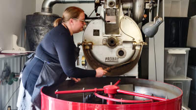 En kvinna håller i en kaffeskopa intill en kafferost.