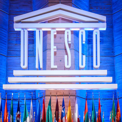 Bild från Unescos generalkonferens 2015. På bilden syns en stor, vit Unesco-logo och medlemsländernas flaggor uppställda framför den.