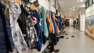 En korridor i en skola. På ena väggen hänger en lång rad med utekläder.