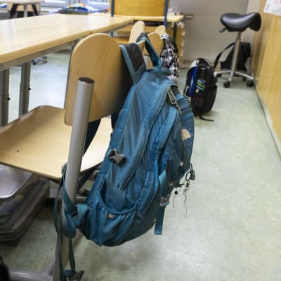 En skolväska hänger över en stolsrygg i ett klassrum.