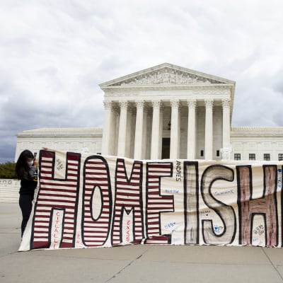 Man och kvinna håller upp skylt där det står ''det här är hemma'' framför USA:s högsta domstol.