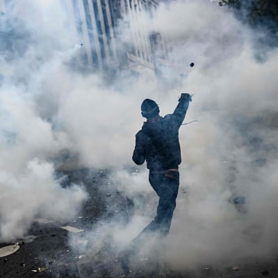 Mielenosoittajat heittävät kiviä kyynelkaasun savussa.