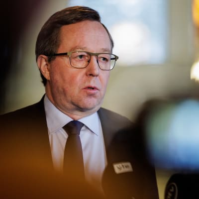 Näringsminister Mika Lintilä, en man i övre medelåldern med grånande hår och glasögon som bär kostym blir intervjuad framför en tv-kamera.