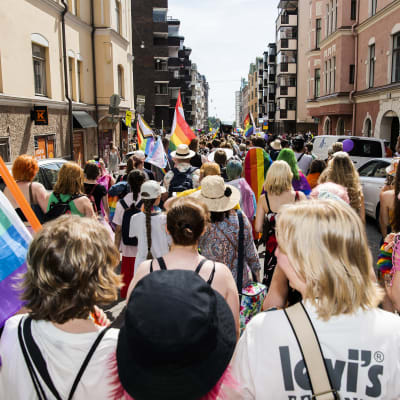 Personer som går i prideparaden i Helsingfors 2022. De har ryggarna vända mot kameran och viftar med regnbågsflaggor.