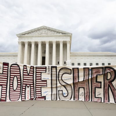 Man och kvinna håller upp skylt där det står ''det här är hemma'' framför USA:s högsta domstol.