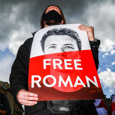 En man i munskydd håller upp en skydd där det står "fria Roman".