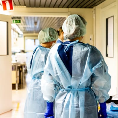 Sjukskötare i skyddsmundering står i en korridor och förbereder sig på att föra coronapatienter till isolering.
