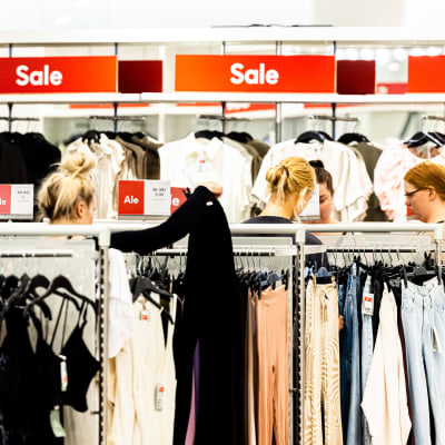 Kvinnor mellan klädhyllorna under en rea-försäljning. 