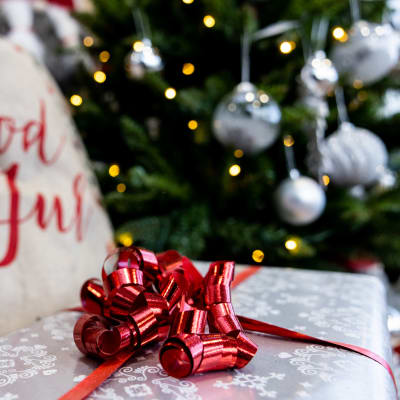 Ett paket med julpapper på syns i förgrunden. I bakgrunden syns en dyna där det står "god jul" samt en julgran.