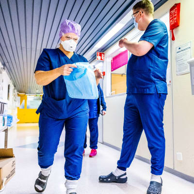 Två vårdare med munskydd går i en korridor.