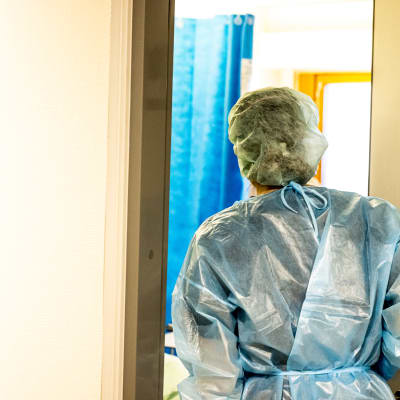 En vårdare iklädd skyddsutrustning går in i ett patientrum.