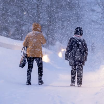 Två personer går i kraftigt snöfall. 