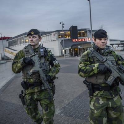 Två tungt beväpnade svenska soldater patrullerar utanför en hamnterminal. 