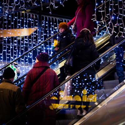 Människor åker rulltrapport i ett köpcentrum pyntat med julljus.